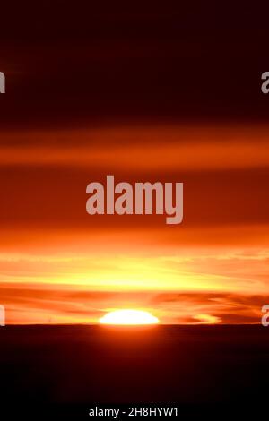 Moitié de soleil visible au-dessus de la mer en jetant un faisceau orange de lumière dans les nuages au-dessus Banque D'Images