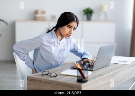 Fatiguée contrariée jeune employée hindoue souffrent de douleurs dorsales sur le lieu de travail à l'intérieur du bureau, se sentant mal Banque D'Images