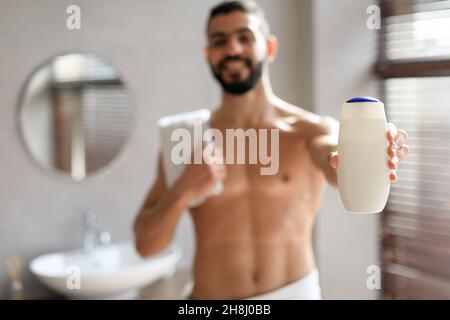Beau jeune homme debout avec une bouteille de shampooing dans les mains Banque D'Images