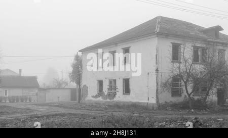 Une maison en bois abandonnée de deux étages au bord de la route par un jour brumeux, photo en noir et blanc Banque D'Images