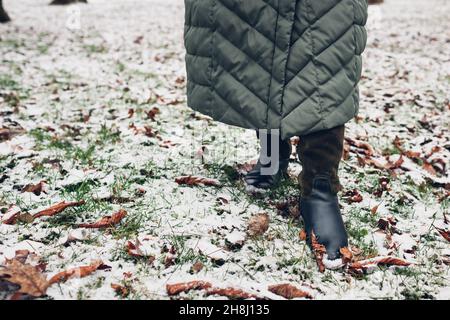 Gros plan des chaussures d'hiver pour femme.Femme marchant dans un parc enneigé avec un long manteau chaud et des bottes hautes en daim vert Banque D'Images