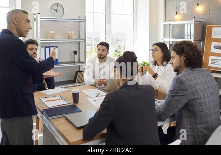 Le cadre supérieur donne des instructions aux jeunes employés lors d'une réunion d'affaires à une table dans un bureau moderne. Banque D'Images