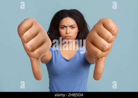 Femme noire sérieuse montrant le pouce sur fond bleu de studio Banque D'Images