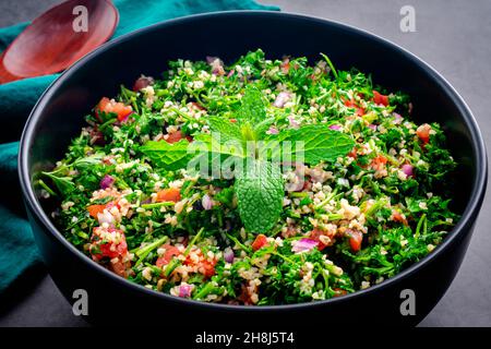 Tabouleh libanais authentique garni de feuilles de menthe : un grand bol de salade de persil avec boulgour, tomates et oignons Banque D'Images