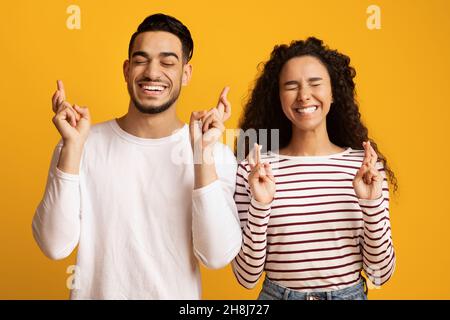 Joyeux jeune couple arabe croiser les doigts, faisant le souhait avec les yeux fermés Banque D'Images