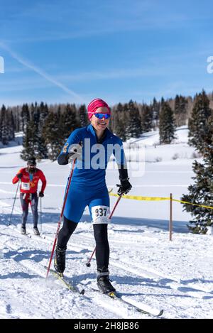 Une femme en vêtement de ski bleu vif, un numéro de course sur sa jambe, ski de fond à travers un pré couvert de neige dans la Chama Chile ski Classic. Banque D'Images