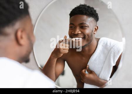 Black Man regardant son sourire dans le miroir dans la salle de bains Banque D'Images