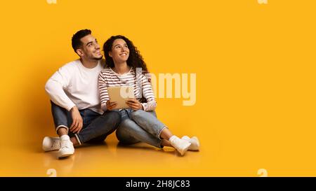 Couple du Moyen-Orient assis avec une tablette numérique et regardant loin avec intérêt Banque D'Images