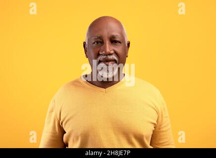 Portrait d'un homme noir âgé heureux regardant l'appareil photo sur fond orange studio Banque D'Images