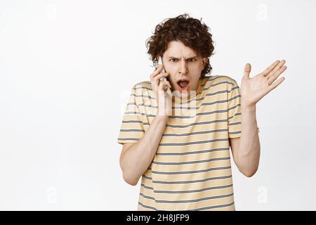 L'image d'un jeune homme reçoit un appel téléphonique, gassing et l'air choqué après avoir entendu quelque chose de terrible, debout sur fond blanc Banque D'Images