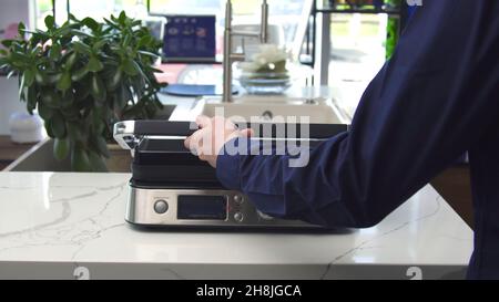 Presse-gril électriqueUstensiles ménagers.Gros plan de l'homme soulevant le couvercle du tout nouveau gril électrique.Design moderne avec corps en métal pour gril électrique pr Banque D'Images