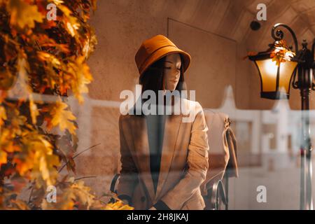 Mannequin féminin habillé d'un élégant chapeau orange et d'une veste beige.Collection automnale sur la boutique de vitrines. Banque D'Images
