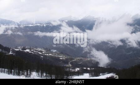 Vue de dessus du paysage de montagne et petit complexe d'hiver.Des nuages sombres qui se profilent au-dessus des sommets et des contreforts de la station d'hiver par temps enneigé. Banque D'Images