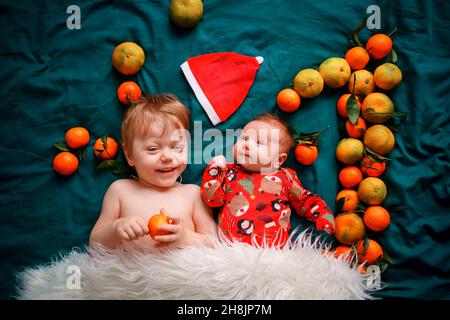 Le frère aîné est avec un nouveau-né de Noël sur un lit vert confortable, à côté du chapeau du Père Noël et le numéro un des mandarines.Les bébés le sont Banque D'Images