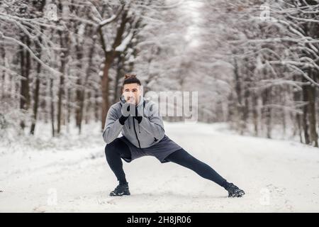 Faites des exercices d'étirement et d'échauffement en forêt par un sportif lors d'une journée hivernale enneigée.Vie saine, échauffement, temps froid Banque D'Images