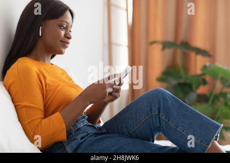Femme afro-américaine utilisant un téléphone portable et portant des écouteurs sans fil à la maison Banque D'Images