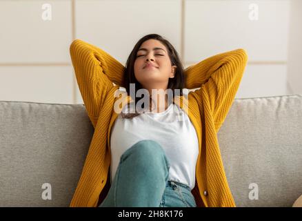 La vie est bonne.Jeune arabe penchée sur un canapé avec les yeux fermés et les mains derrière la tête, reposant sur un canapé à la maison Banque D'Images