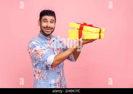 Joyeux homme excité avec la barbe tenant dans les mains moitié ouvert jaune emballage boîte cadeau, regardant la caméra avec excitation et surprise.Studio d'intérieur isolé sur fond rose. Banque D'Images