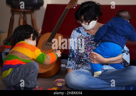 femme avec masque mains guitare à l'enfant tout en tenant bébé dans les bras. jeux pandémiques à la maison. covid-19 coronavirus Banque D'Images