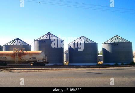 Le train rouillé se trouve devant une série de silos à grains sur une route de l'arrière-pays Banque D'Images