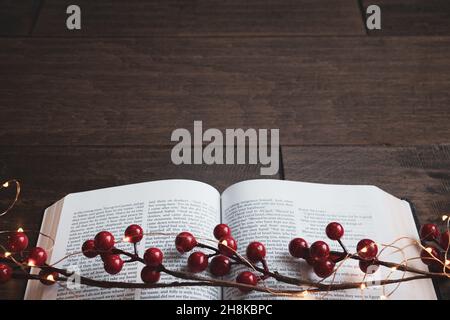 Guirlande de baies rouges et guirlande de mini-guirlandes de noël sur une bible ouverte sur un fond de bois sombre avec espace de copie Banque D'Images