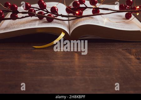 Guirlande de baies rouges et guirlande de mini-guirlandes de noël sur une bible ouverte sur un fond de bois sombre avec espace de copie Banque D'Images