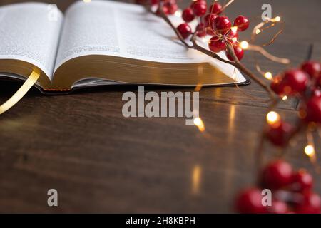 Guirlande de baies rouges et guirlande de mini-guirlandes de noël sur une bible ouverte sur un fond de bois sombre avec espace de copie Banque D'Images