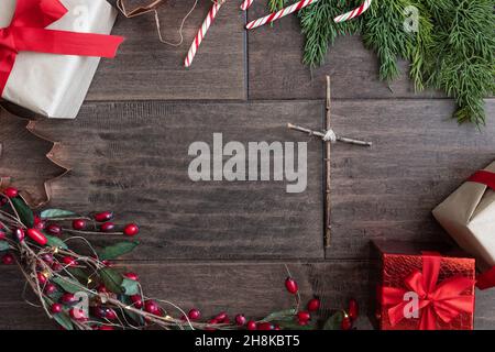 Cadre de Noël en cadeau, Cannes en sucre, creux à feuilles persistantes en rouge et vert avec une simple croix chrétienne avec un espace de copie sur fond de bois sombre Banque D'Images