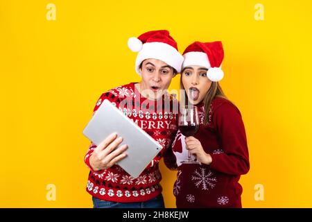 jeune couple latin ayant des appels vidéo de noël à l'aide d'une tablette numérique ou d'un pavé tactile sur un fond jaune en amérique latine Banque D'Images