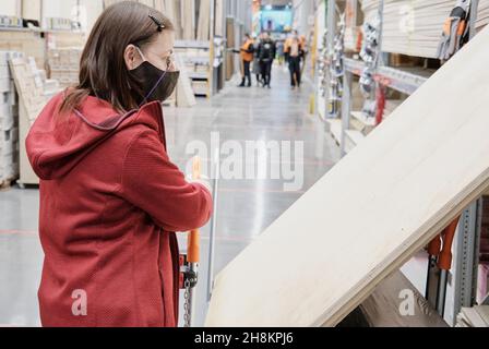 Femme dans le magasin de matériaux de construction, elle tient le chariot sur lequel une énorme feuille de contreplaqué Banque D'Images