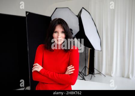 Femme sérieuse dans le col de cygne rouge debout avec les mains pliées en studio avec l'équipement pour séance de photo et regarder la caméra Banque D'Images