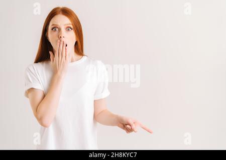 Studio portrait de la jeune femme terrifiée couvrant la bouche recommander suggère de sélectionner l'index de point de publicité de côté sur un fond blanc isolé Banque D'Images