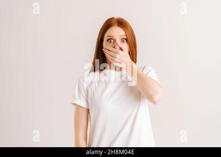 Portrait en studio d'une jeune femme choquée et stupéfait couvrant la bouche avec des paumes pressées qui se succissent aux yeux de la caméra de la surprise et de l'inquiétude Banque D'Images