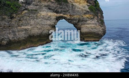 Les vagues se brisent sur la rive d'une falaise pierreuse Batu Madeg ou Nusa Batu Melawang avec une fissure au milieu Banque D'Images