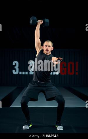 Fort brutal homme faisant des squats avec haltère à la salle de gym, pleine photo.Guy faisant des exercices avec haltères à l'intérieur. Banque D'Images