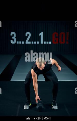 Fort brutal homme faisant des squats avec haltère à la salle de gym, pleine photo.Guy faisant des exercices avec haltères à l'intérieur. Banque D'Images