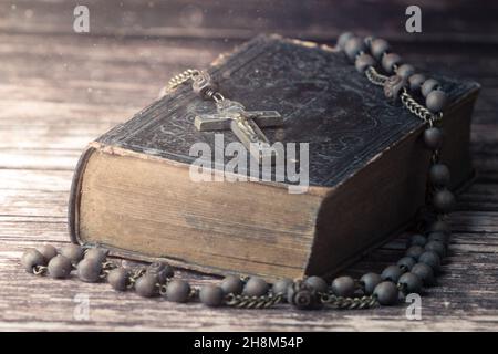 Studio de détail tourné de très ancienne, ancienne Sainte Bible avec beaucoup d'ornements sur la couverture et les pages jaunes et vieux rosaire sur le bureau en bois vintage Banque D'Images