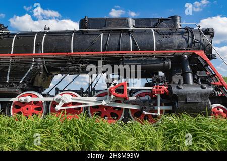 Gros plan de l'avant d'une locomotive à vapeur arrêtée derrière l'herbe verte contre un ciel bleu Banque D'Images