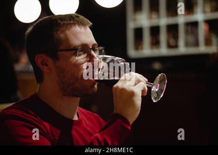 Un jeune homme dans un restaurant boit du vin rouge à partir d'un verre Banque D'Images