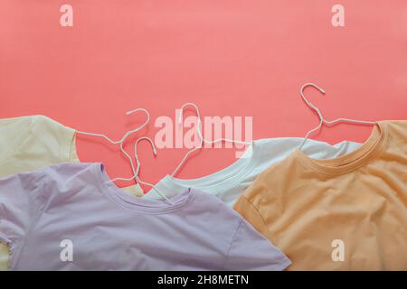 T-shirts multicolores sur cintres couleurs pastel beige blanc violet.T-shirts maquette sur fond rose corail.T-shirts empilés de base vêtements Banque D'Images