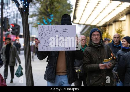 Un militant du vaccin contre le coronavirus tient une affiche le long d'Oxford Street pendant la construction jusqu'à Noël 2021 et l'augmentation des cas de COVID 19 au Royaume-Uni. Banque D'Images