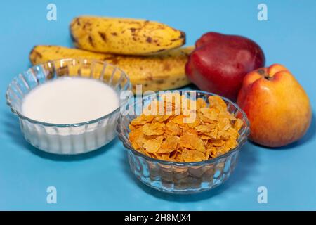 Régime sain de petit déjeuner de flocons de maïs avec du lait et des fruits en gros plan sur fond bleu Banque D'Images