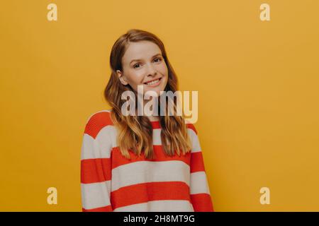 Jeune femme heureuse avec de longs cheveux ondulés se sentant incroyable, regardant l'appareil photo avec le sourire chaleureux mignon Banque D'Images