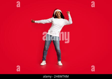 Belle femme noire en chapeau de père Noël dansant sur rouge Banque D'Images