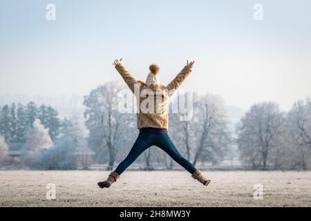 Bonne femme sautant avec les bras étirés dans la nature.Jeune femme insouciante s'amusant à l'extérieur.Profitez de la saison d'hiver et du temps froid Banque D'Images