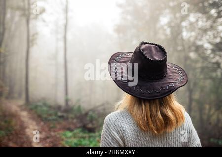 Touriste avec chapeau regardant le brouillard dans la forêt pendant la randonnée.Explorer randonnée dans les bois d'automne.Femme portant un chandail tricoté et un chapeau de cow-boy Banque D'Images