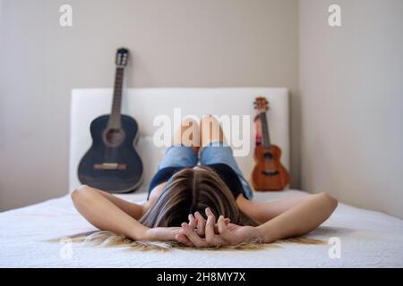 Femme avec instruments au lit. Fille avec sa guitare et son ukulele sur le lit dans sa chambre à la maison. Guitare espagnole. Banque D'Images