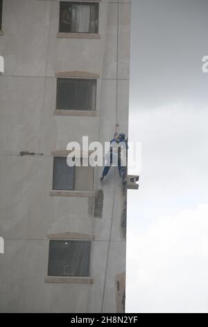 salvador, bahia, brésil - 30 novembre 2021 : ouvrier de la construction suspendu avec des cordes sur une façade d'un bâtiment pendant les travaux de construction dans la ville Banque D'Images