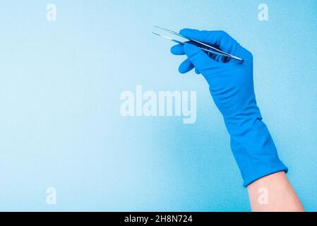 Main dans un gant bleu tenant une pince à épiler dentaire Banque D'Images