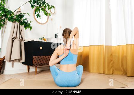 Vue arrière de la belle jeune femme pratiquant le yoga à l'intérieur.Femme pratique dans la salle de bain légère.Plantes de maison. Banque D'Images